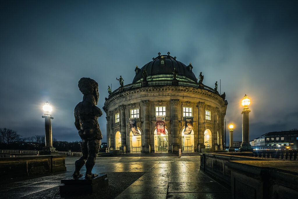 Blick auf das Bode-Museum in Berlin bei Nacht, mit einer Statue im Vordergrund und beleuchteten Fenstern, die Kunstwerke präsentieren.