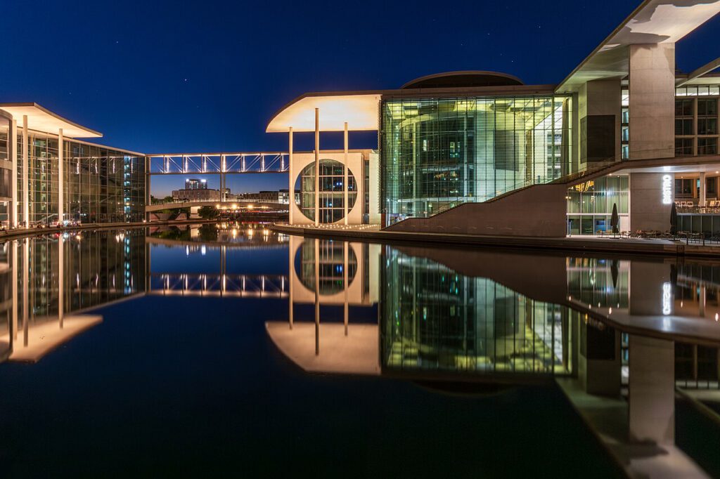 Moderne Architektur der Regierungsviertel in Berlin bei Nacht, reflektiert im Wasser, mit beleuchteten Glasfassaden und einem futuristischen Übergang.