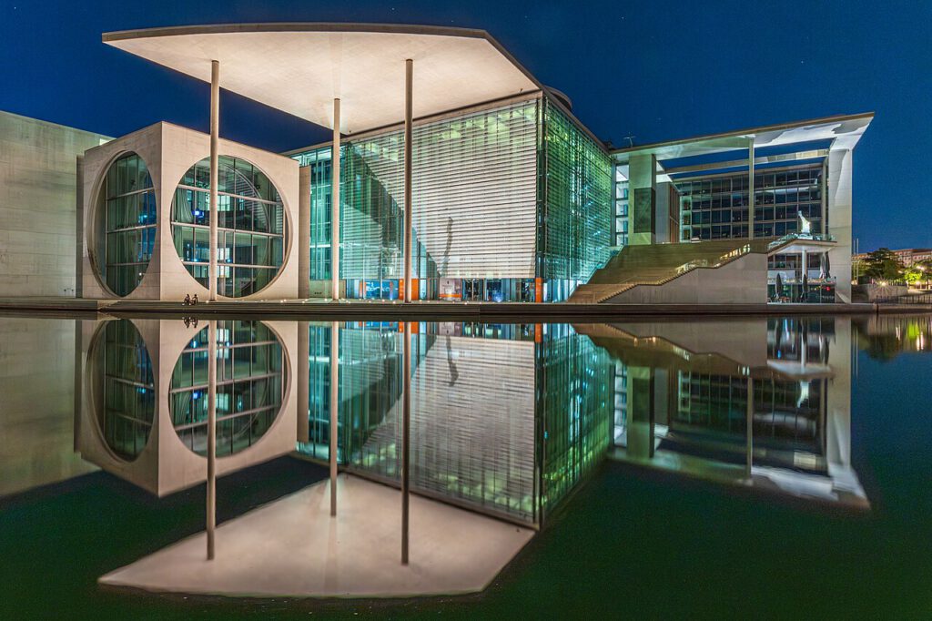 Moderne Architektur des Bundeskanzleramts in Berlin bei Nacht, reflektiert im Wasser. Die markanten geometrischen Formen und das Lichtspiel betonen das zeitgenössische Design des Gebäudes.