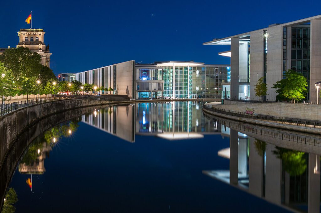 Berlin Regierungsviertel bei Nacht, Blick auf den Spreefluss mit reflektierenden Gebäuden, darunter das Bundeskanzleramt und der Reichstag.
