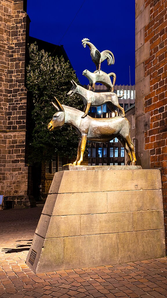 Das Denkmal der Bremer Stadtmusikanten am Bremer Rathaus. Aufgenommen zur blauen Stunde. Das Denkmal, bestehend aus Esel, Hund, Katze und Hahn, die in dieser Reihenfolge aufeinander stehen, wird angeleuchtet und hebt sich so vom Hintergrund ab.