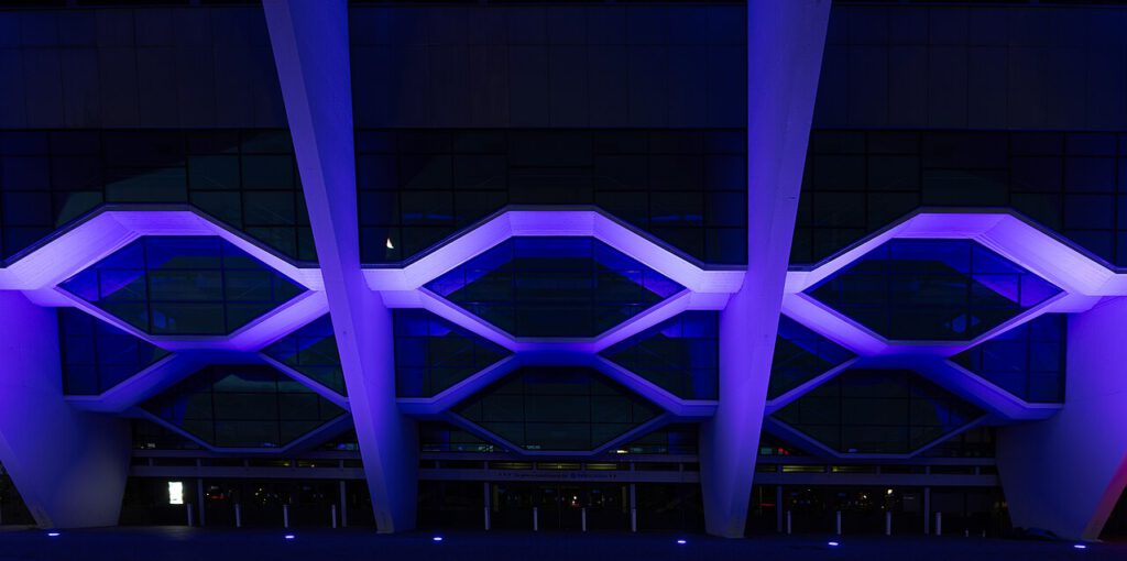 Abstrakt wirkende Detailaufnahme der Stadthalle in Bremen bei Nacht. Zu sehen ist der Eingangsbereich, dessen Fenster an Bienenwaben erinnern.