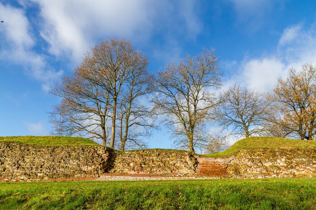 Auf dem Bild ist ein Teilstück der Ziegelmauer der Waldemarsmauer zu sehen, die Teil des Danewerkes ist. Hinter dem Wall wachsen Bäume, davor ist ein gepflegter Rasen.