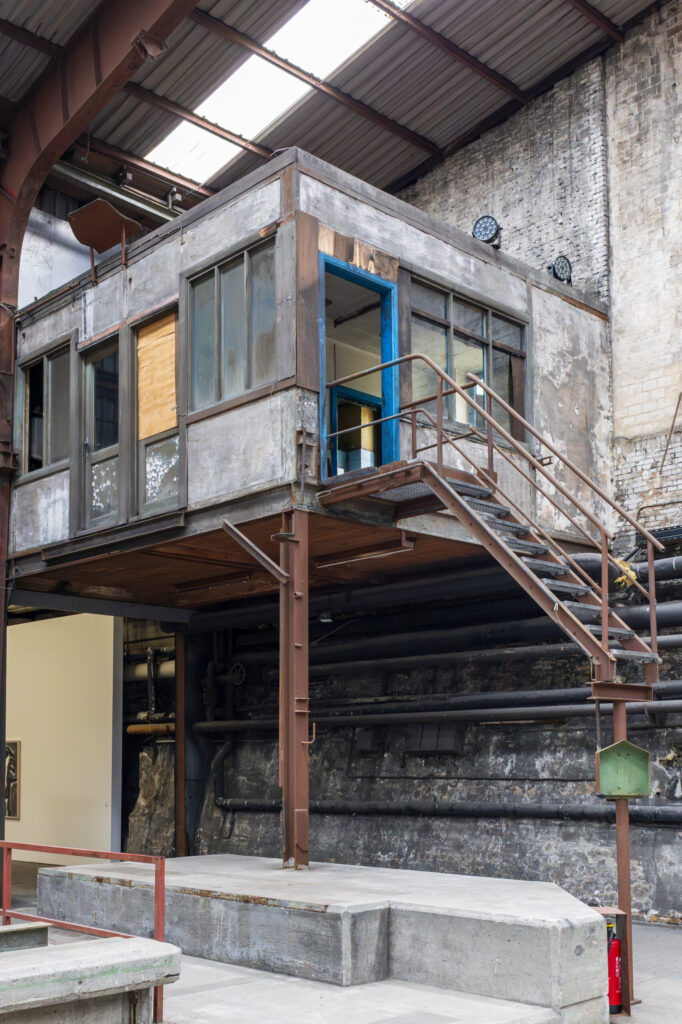 lick in die Werkshalle der Carlshütte, die wie ein Lost Place wirkt. Zu sehen ist ein erhöhter Raum, aus dem eine Treppe führt, die auf halber Höhe abgeschnitten ist.