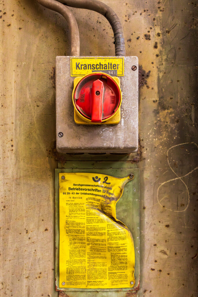 Alte Schalter in der Werkshalle der Carlshütte, die wie ein Lost Place wirkt. Darunter ein angeschmolzenes Schild mit Sicherheitsanweisungen.