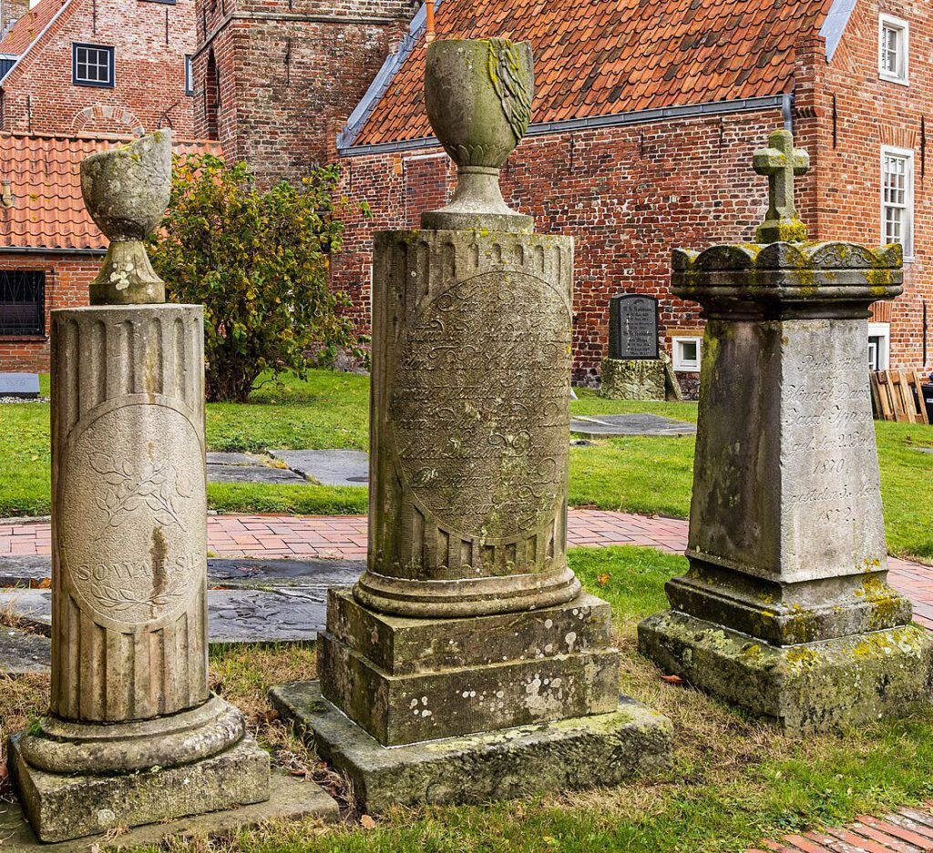 Drei historische Grabsteine auf dem Friedhof von Greetsiel. Zwei sind mit viel Text beschrieben, auf einem finden sich nur drei Worte.