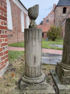 Bild des Grabsteines von Antje Hinderika Ippen auf dem Friedhof von Greetsiel. Der Stein ist säulenförmigt und vn einer zerbrochenen Vase bekrönt.