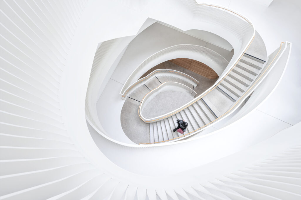 Geschwungenes Treppenhaus, fotografiert von Marion Liebmann: Die elegante Spiralform wird durch die Anwesenheit eines Menschen auf der Treppe hervorgehoben, was die beeindruckende Dimension und architektonische Ästhetik unterstreicht.