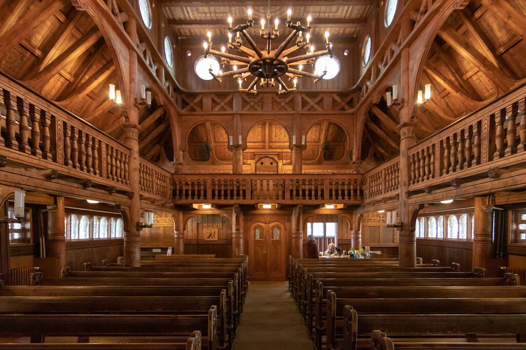 Innenraum der Stabkirche, in warmes Licht getaucht, mit einer vollständig aus Holz gefertigten Architektur. Die Emporen und die kunstvollen Holzverzierungen verleihen dem Raum eine gemütliche, sakrale Atmosphäre.