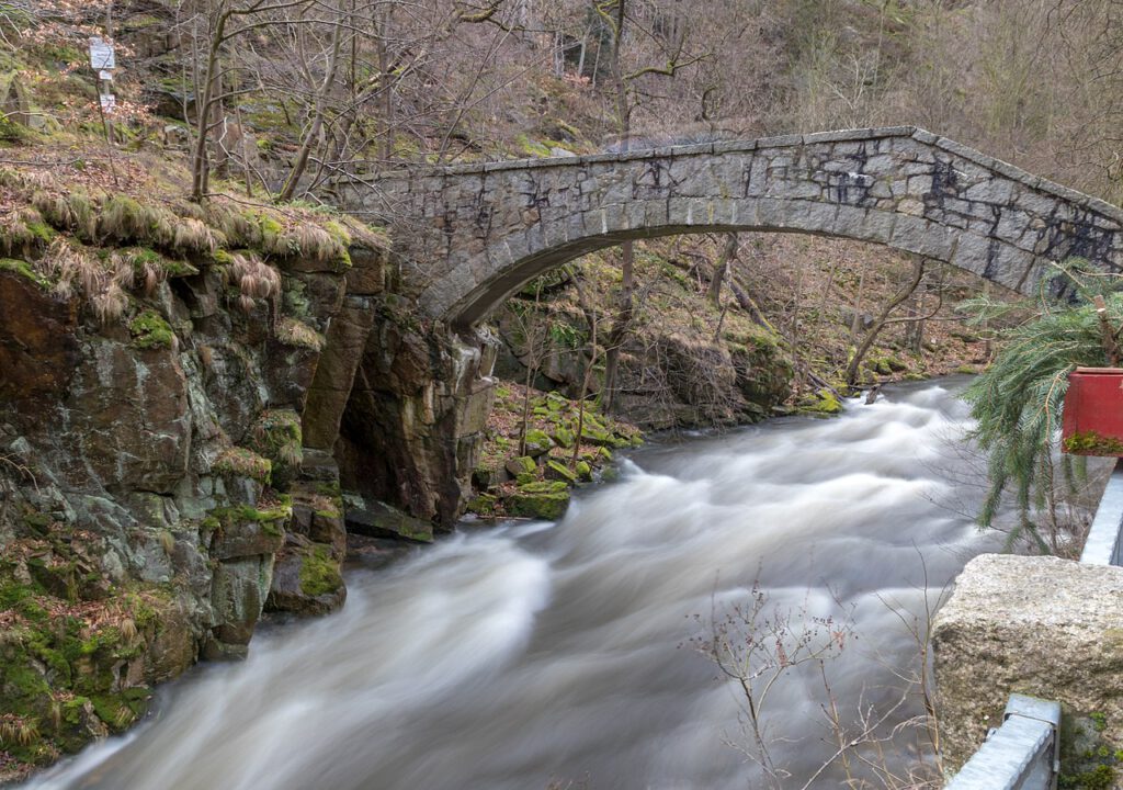 Die Jungfernbrücke über die Bode bei Thale, aufgenommen in einer Langzeitbelichtung. Das fließende Wasser der Bode erscheint weich und glatt, während die Brücke und die umliegende Landschaft klar und detailreich hervortreten. Eine stimmungsvolle Aufnahme mit ruhiger Atmosphäre.