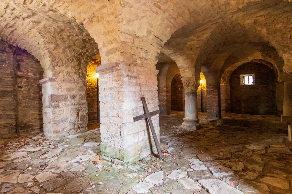 Ein historisches Kellergewölbe in Drübeck mit einer massiven Steinarchitektur. An eine der Säulen ist ein Kreuz gelehnt, das eine spirituelle und zeitlose Atmosphäre im Raum schafft