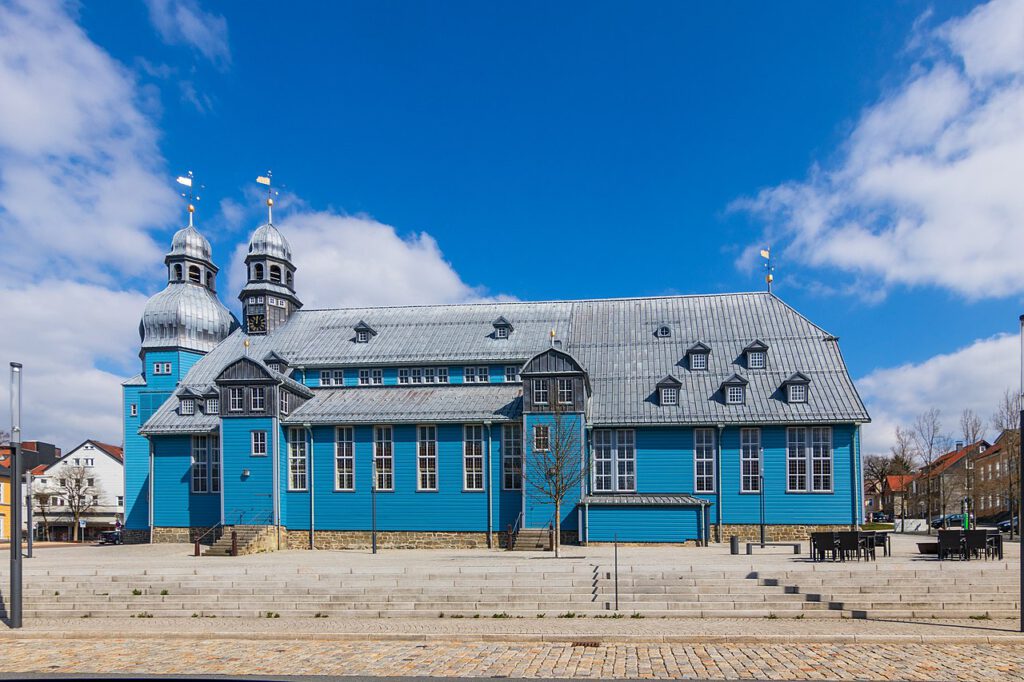 Außenaufnahme der Marktkirche zum Heiligen Geist in Clausthal, die größte Holzkirche Deutschlands. Das Gebäude ist auffällig blau angestrichen und zeichnet sich durch seine beeindruckende Holzarchitektur und die markanten Türme aus.