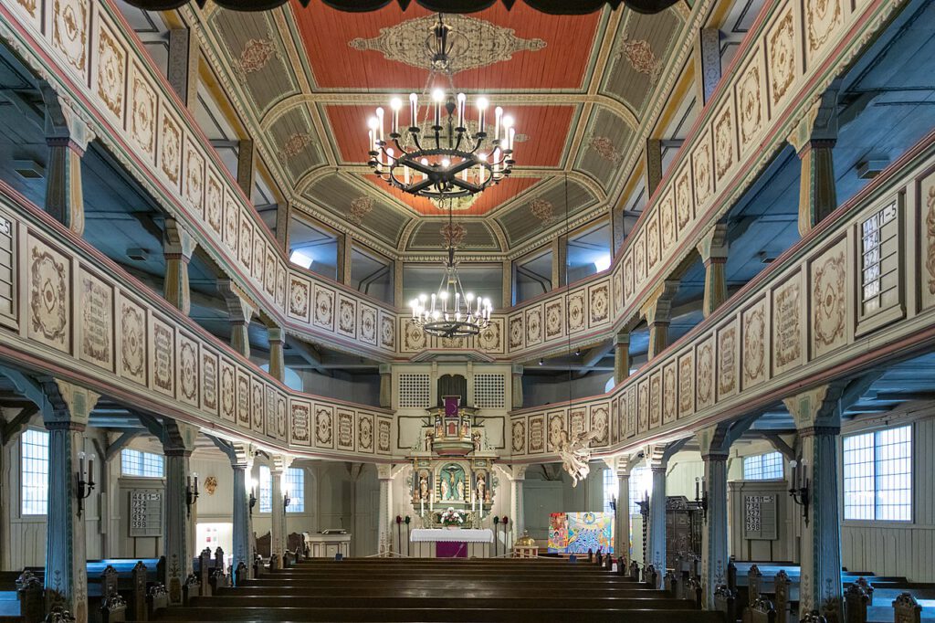 Innenaufnahme der Kirche St. Andreas in Bad Lauterberg, mit prächtiger Holzarchitektur. Zwei übereinander angeordnete Emporen erstrecken sich entlang der Wände, wobei die feinen Holzverzierungen und die majestätische Raumgestaltung eine beeindruckende Atmosphäre schaffen.