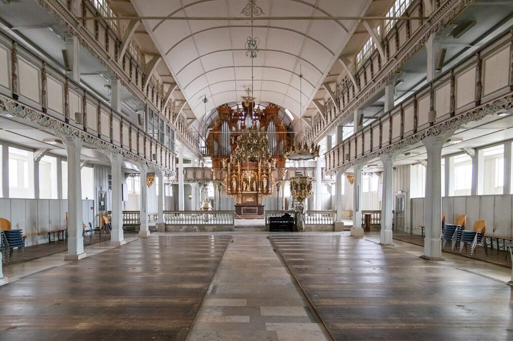 Innenaufnahme der Marktkirche zum Heiligen Geist in Clausthal, der größten Holzkirche Deutschlands. Der weite Innenraum ohne Bestuhlung wirkt offen und luftig, mit der markanten Holzarchitektur, die den Raum in einem warmen, natürlichen Licht erstrahlen lässt.