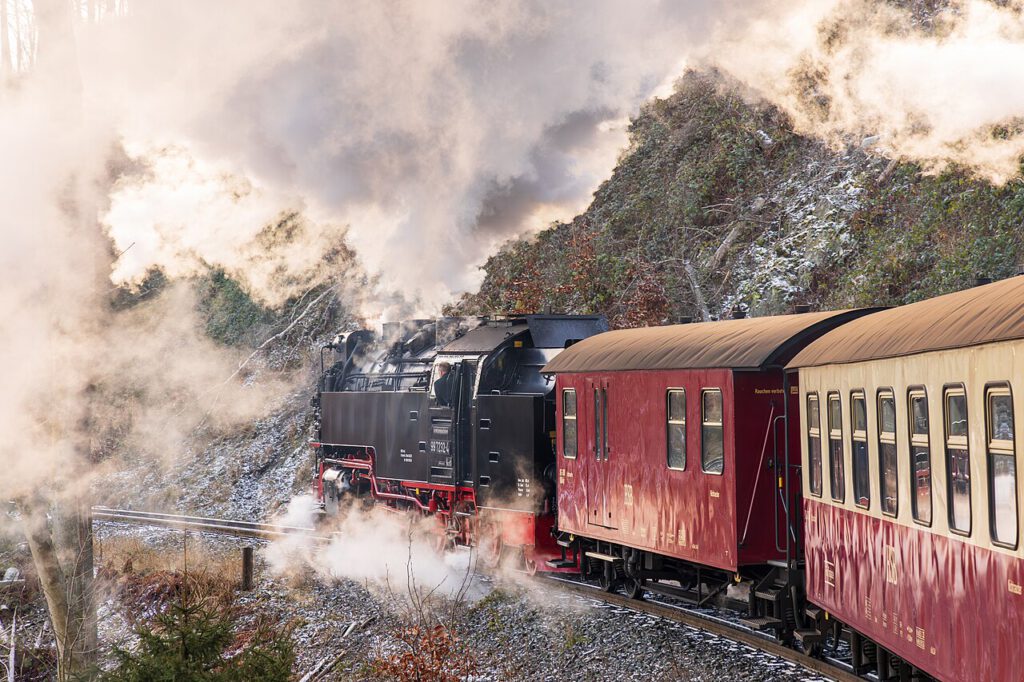 Die Brockenbahn dampft auf ihrem Weg zum verschneiten Brockengipfel. Dichter weißer Dampf steigt aus der Lokomotive auf, während die Landschaft in Schnee gehüllt ist und eine winterliche Stimmung vermittelt.