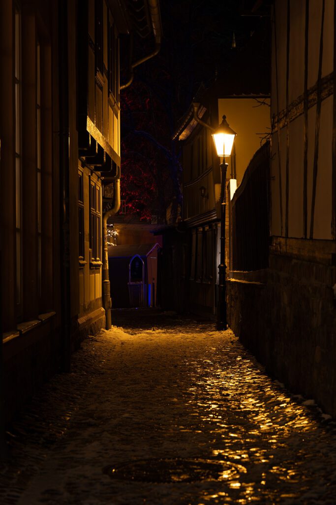 Nachtaufnahme einer schwach beleuchteten Kopfsteinpflasterstraße in Wernigerode. Die sanfte Straßenbeleuchtung taucht die steinerne Straße in ein gedämpftes Licht, während die historische Architektur entlang des Weges die Szenerie prägt