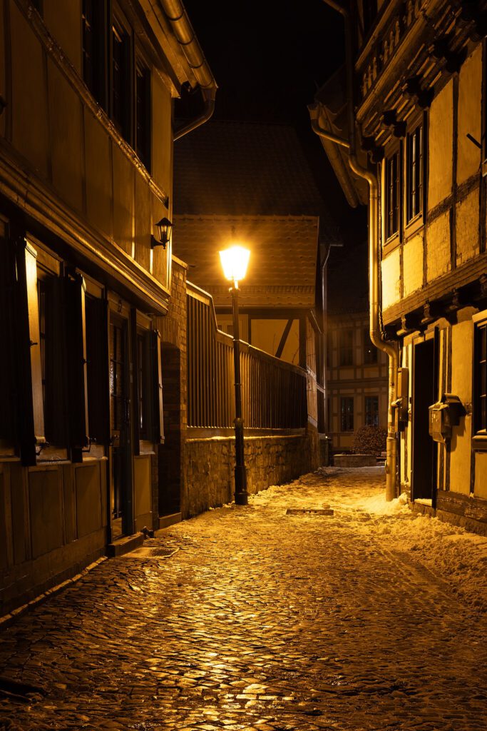 Nachtaufnahme einer schwach beleuchteten Kopfsteinpflasterstraße in Wernigerode. Eine einzelne Straßenlaterne spendet schwaches Licht und wirft sanfte Schatten auf die Pflastersteine, wodurch eine ruhige und nostalgische Atmosphäre entsteht.