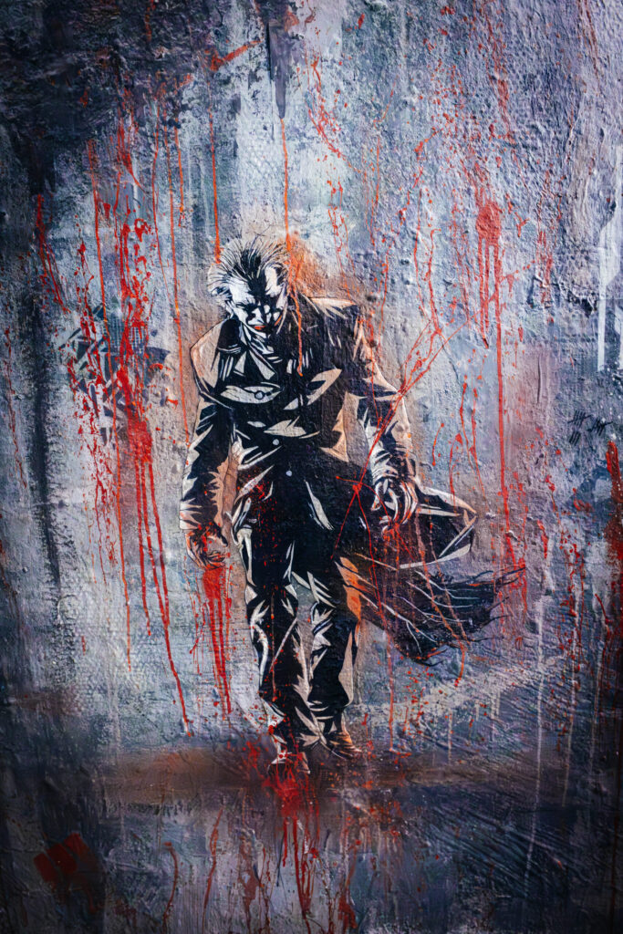 Streetart eines düster wirkenden Mannes im langen Mantel, inspiriert vom Joker-Charakter, auf einer rauen, teils beschädigten Wand. Die Figur ist in dunklen Tönen gehalten, mit kontrastreichen weißen Konturen. Der Hintergrund ist in Grau- und Blautönen gehalten, überzogen mit roten Farbspritzern und Tropfen, die an Blut erinnern. Die Szene wirkt dramatisch, bedrohlich und emotional aufgeladen – typisch für urbane Underground-Kunst wie sie im ehemaligen Kunsthaus Tacheles in Berlin zu finden ist.