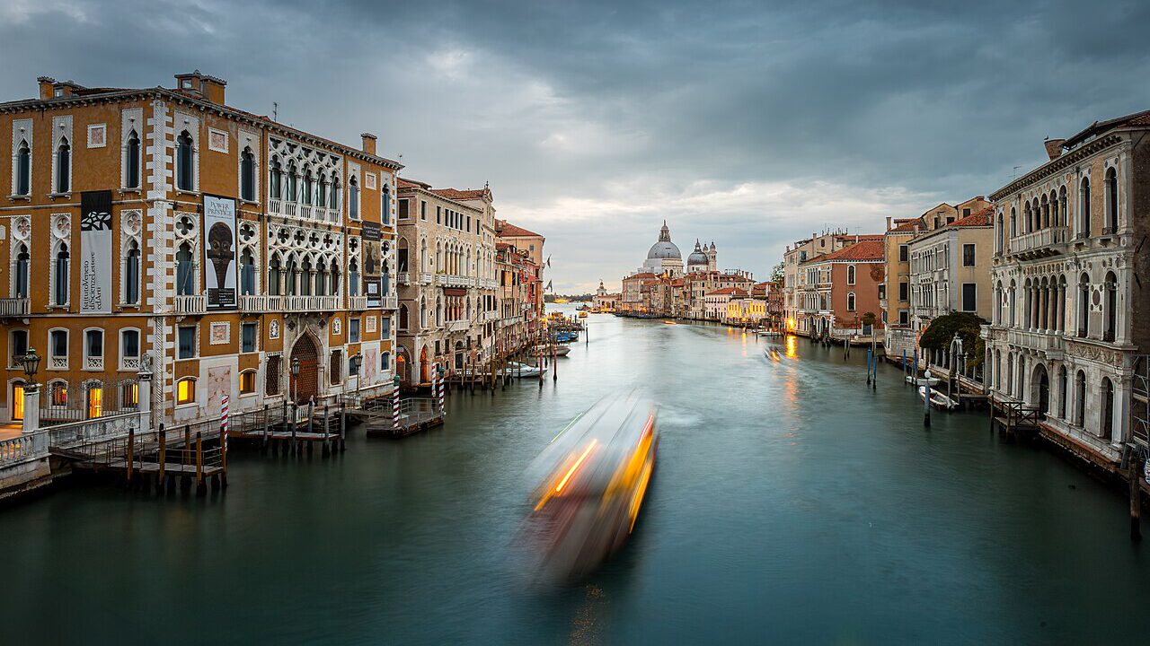 Venedig Kanal mit historischen Gebäuden und einem vorbeifahrenden Boot unter einem bewölkten Himmel, ideal für Reisefotografie und Stadtansichten.