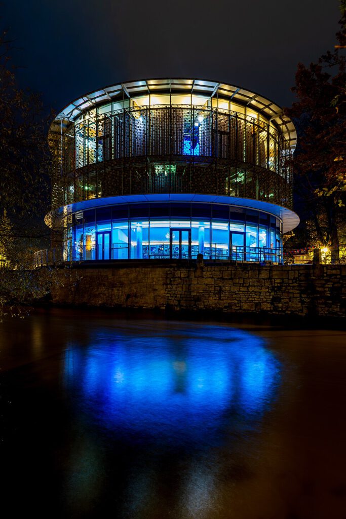 Moderne Architektur des lichtdurchfluteten Gebäudes am Wasser mit blauer Beleuchtung, das nachts leuchtet und eine stilvolle Atmosphäre schafft.