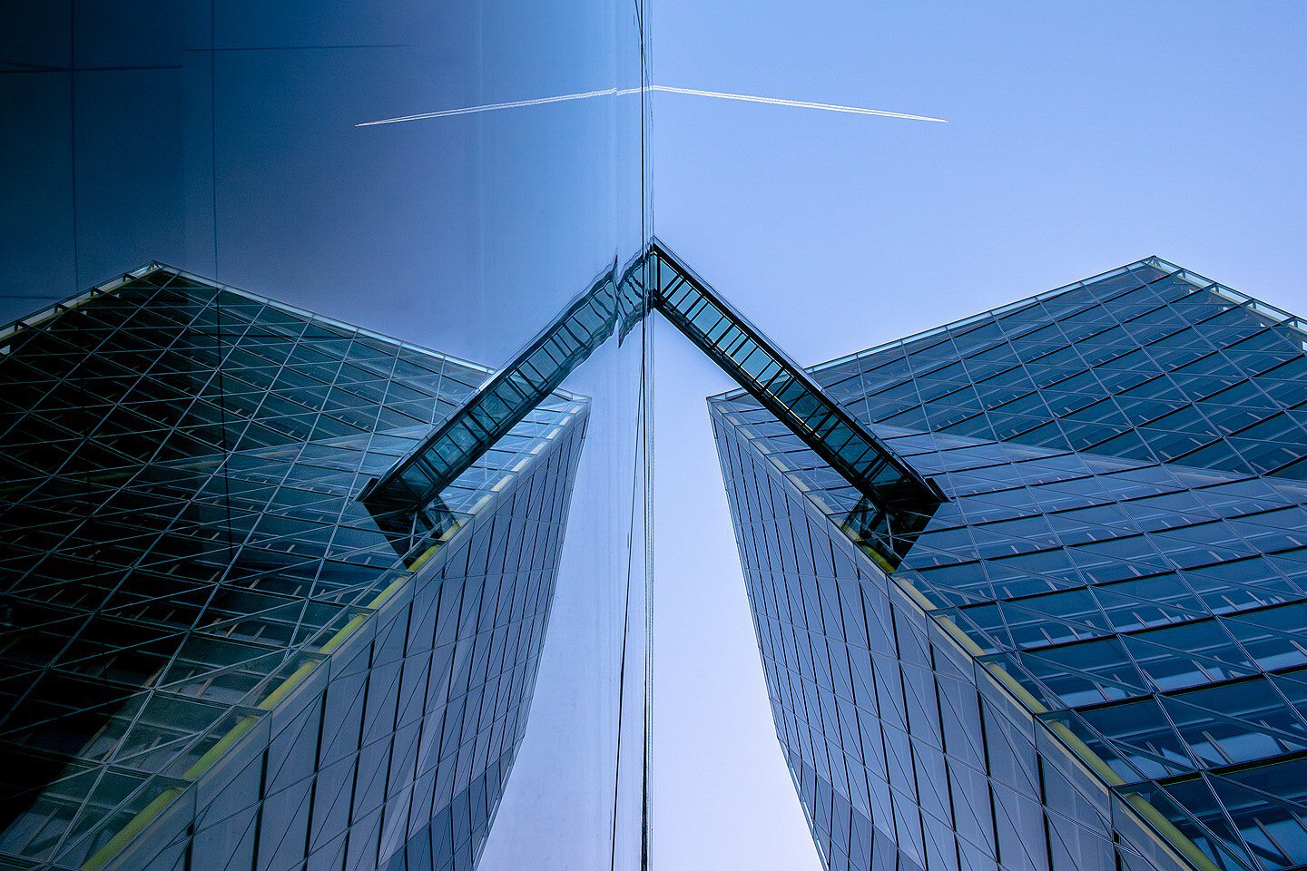 Moderne Architektur eines Hochhauses mit Glasfassade, reflektiert im Wasser, unter einem klaren blauen Himmel mit einem Flugzeug am Horizont.