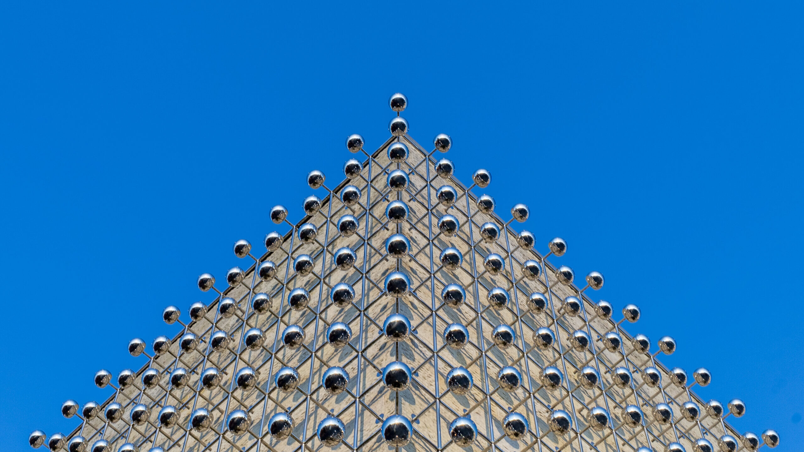 Detailaufnahme der oberen Spitze eines modernen Gebäudes mit glänzenden Kugeln und einem klaren blauen Himmel im Hintergrund.