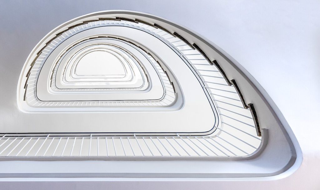 Treppenhaus mit geschwungenen Linien und hellen Wänden, die eine moderne Architektur darstellen. Die Stufen und Geländer sind in einem minimalistischen Design gehalten, was eine elegante und luftige Atmosphäre schafft.