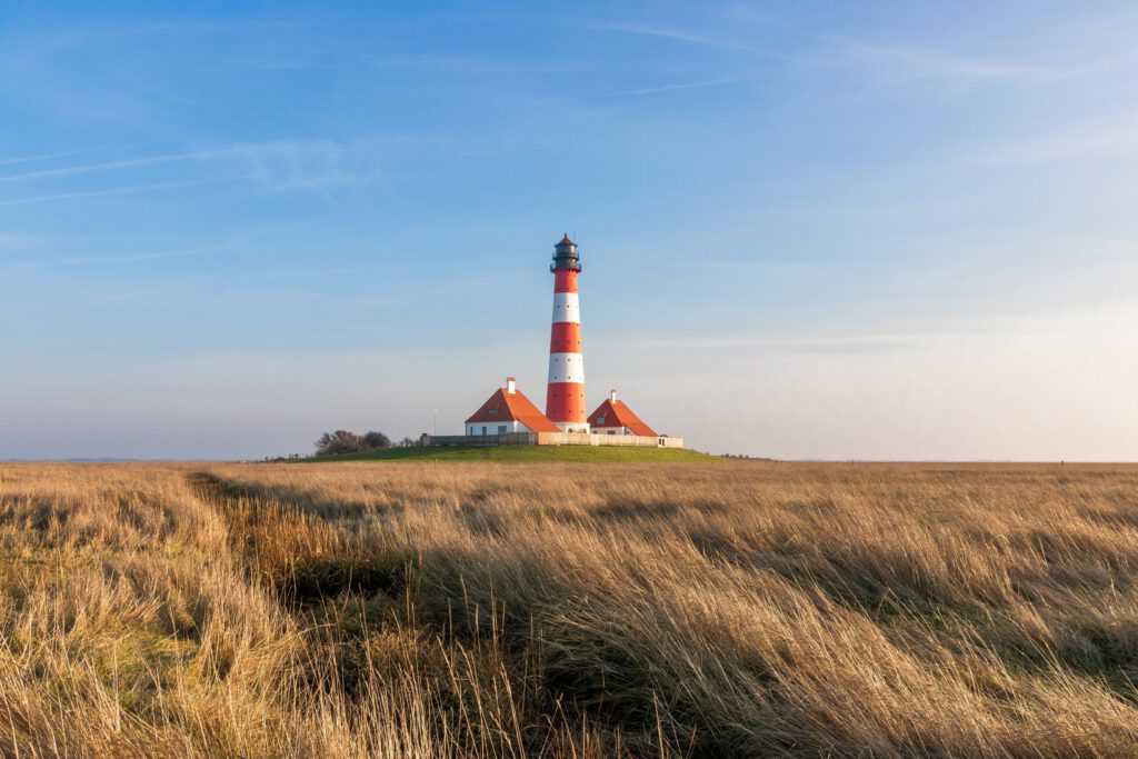 Leuchtturm in der Nordsee mit rot-weißer Streifenmuster, umgeben von weiten Graslandschaften und klarem Himmel. Ideal für maritime Fotografie und Tourismus in Deutschland.